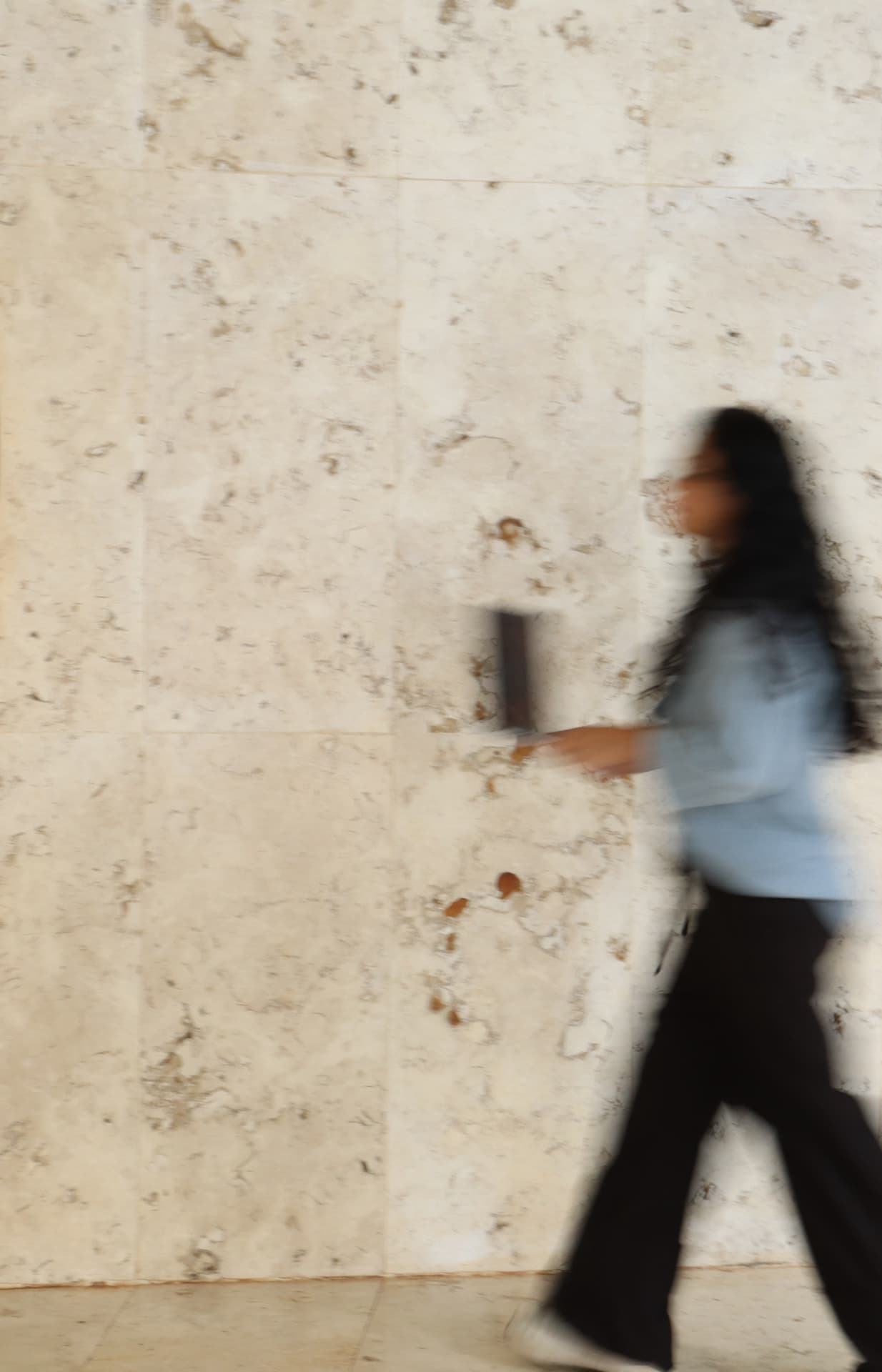 Maeli Galdino caminhando, em movimento, diante de uma parede de pedra